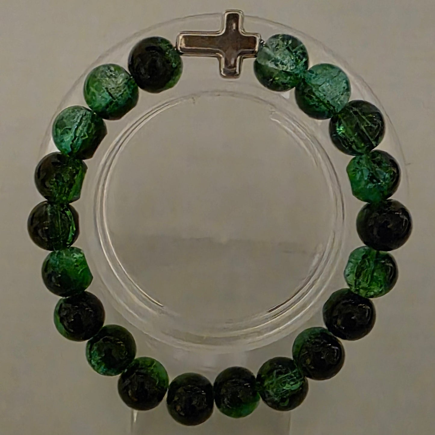 Green beaded bracelet with a silver cross on a white background