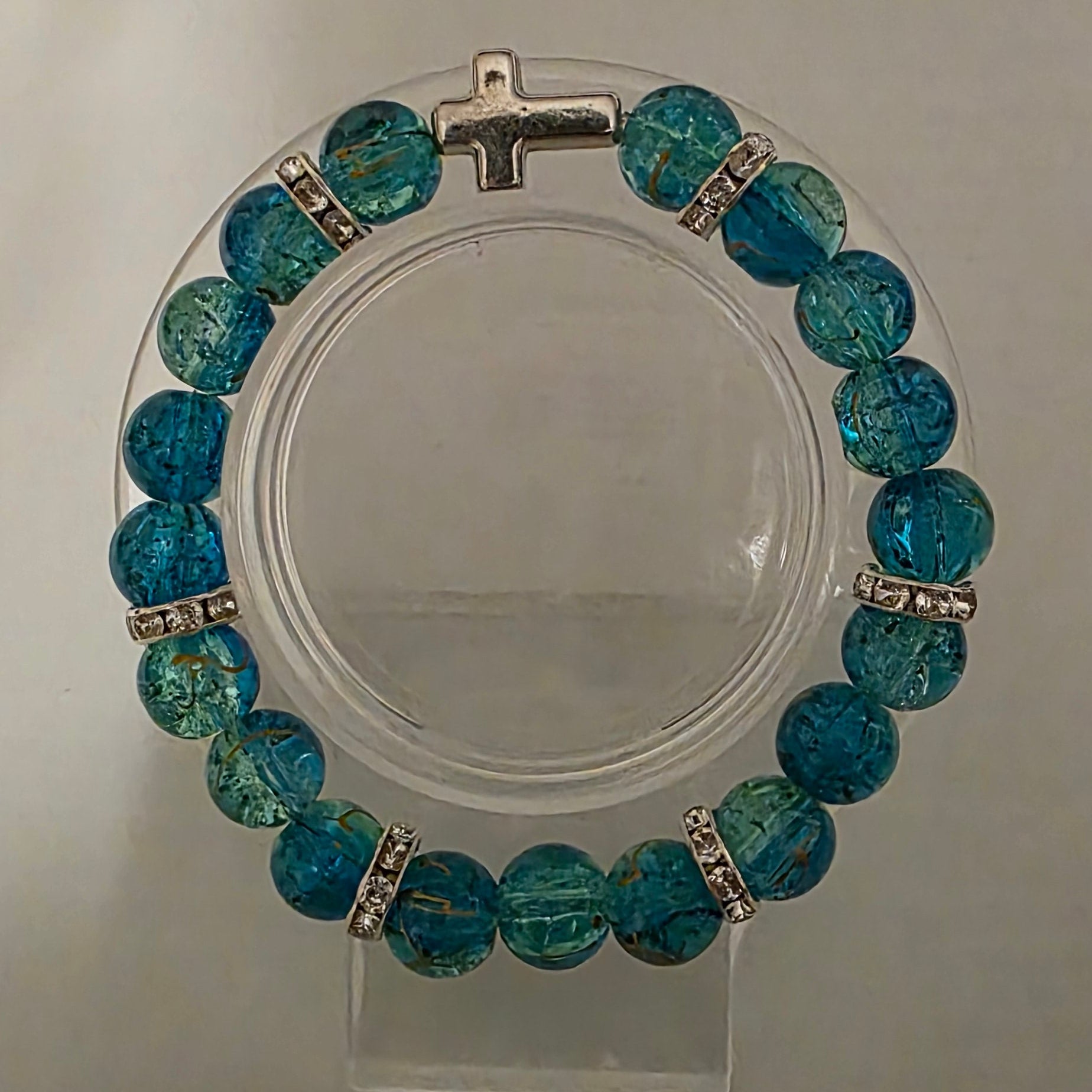 Blue beaded bracelet on a clear stand against a gray background