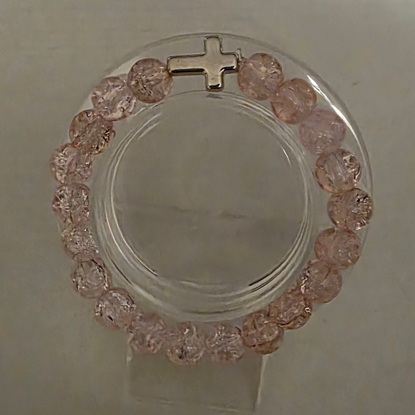Bracelet with pink stones and a cross on a light gray background