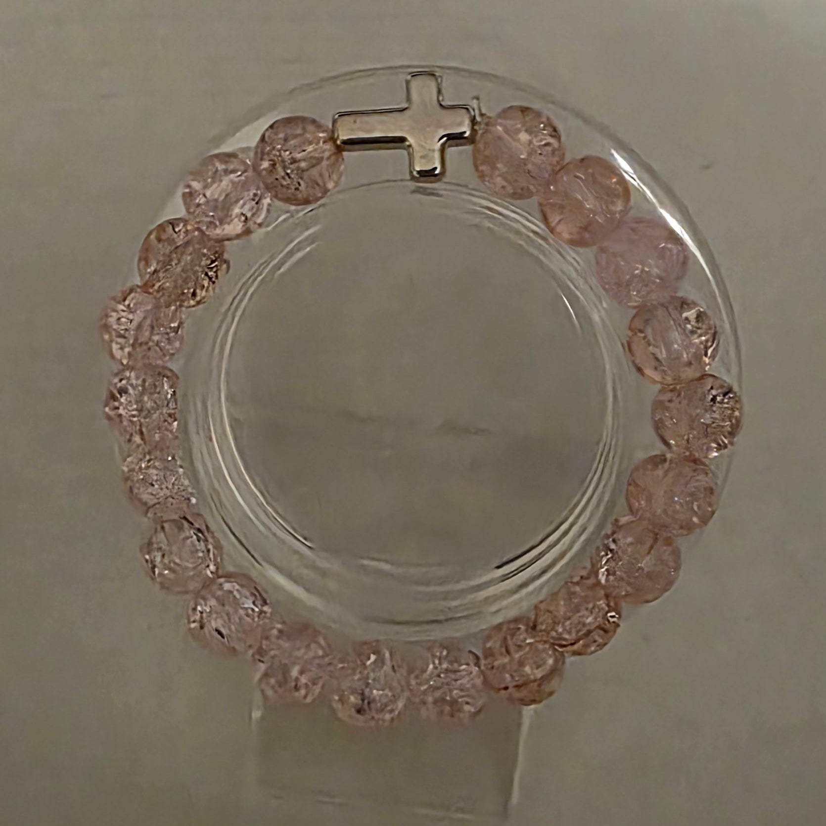 Bracelet with pink stones and a cross on a light gray background
